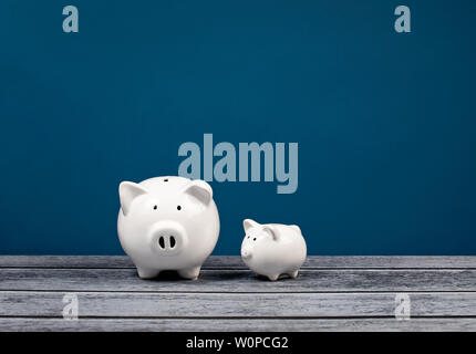 Zwei süße weiße Spardosen über einen blauen und grauen Hintergrund. Familie, Finanzen oder Bank- Konzept. Stockfoto