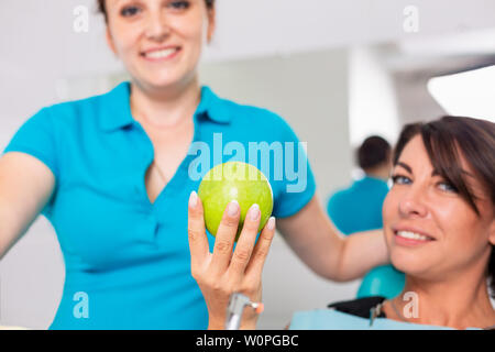 Zahnheilkunde, gesunde Zähne. Zahnarzt gibt grünes Apple zu einem schönen Mädchen, ein Patient die Zähne zu prüfen. Prüfung Zähne mit einem grünen Apfel. Stockfoto