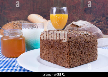 Orangensaft, Joghurt, marmeladenglas und ein Stück Mehrkornbrot auf einem weißen Teller serviert auf einem blauen Tabelle Stockfoto