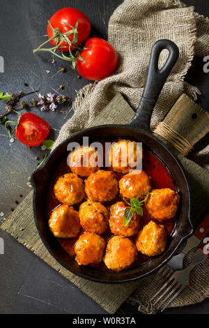 Hausgemachte Frikadellen mit Gewürzen und Tomaten in einer Pfanne auf dunklen Tisch aus Stein. Flach, Ansicht von oben Hintergrund. Stockfoto