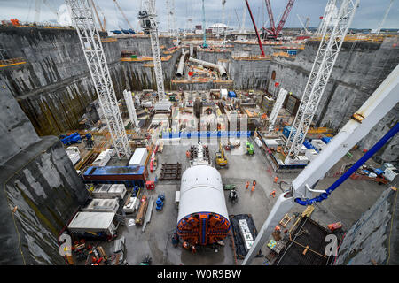 Eine massive Tunnelbohrmaschine im Vordergrund und riesigen kühlwasserleitungen sitzen auf dem tief graben Aushub Kühlkörper in Hinkley Point C, wo Großbritannien, das die größten jemals gießen Beton, rund 9'000 m3, die während der Bau der umgibt, für den Kernreaktor im Kraftwerk in der Nähe von Bridgwater, Somerset. Das gießen Beat das bisher größte, die beim Bau der Shard in London war. Stockfoto