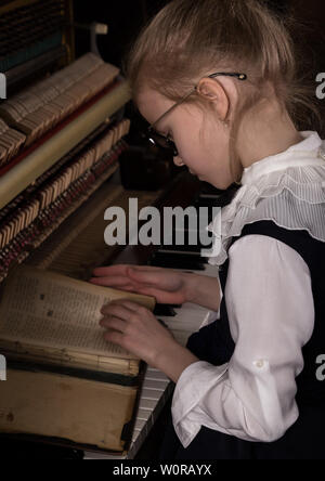 Strenge kleines Mädchen in einem große Gläser Klavier spielen, Kind imitiert Lehrer. Stockfoto