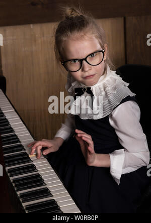 Strenge kleines Mädchen in einem große Gläser Klavier spielen, Kind imitiert Lehrer. Stockfoto