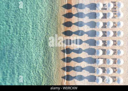 Ansicht von oben, atemberaubenden Blick auf eine erstaunliche leeren weißen Strand mit weißen Sonnenschirmen und türkisklares Wasser während des Sonnenuntergangs. Stockfoto