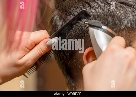 Frau Friseur schneidet die Haare des Mannes mit elektrischer Haarschneider Trimmer. Selektiver Fokus Stockfoto