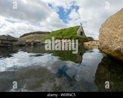 Weitwinkelaufnahme eines Torfhaus und einem geothermischen Hot Pot in Hrunalaug, Island Stockfoto