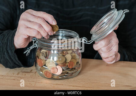 Haende einer alten Frau halten ein Einmachglas mit Kleingeld. Stockfoto