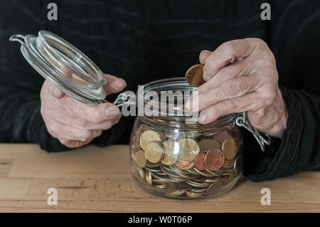 Haende einer alten Frau halten ein Einmachglas mit Kleingeld. Stockfoto