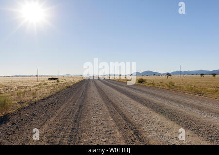 Landschaft mit gerader Straße bis zum Horizont und Sonne, Namibia, Afrika. Stockfoto