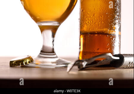 Bier Glas und Flasche auf Holz Tisch mit Flaschenöffner und Verschluss mit weißem Hintergrund. Horizontale Komposition. Vorderansicht. Stockfoto