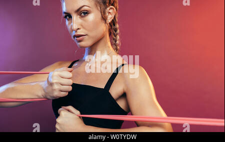 Gesunde Frau, die mit Widerstandsbändern arbeitet. Fitness-Frau dehnt sich mit Widerstandsband vor farbigem Hintergrund. Stockfoto