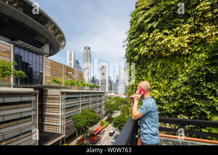 Ein Mann am Telefon bei Urban Farming auf dem Dach der Funan Mall, das Dach bietet Blick auf die Stadtstraße und die modernen Wolkenkratzer in Singapur Stockfoto