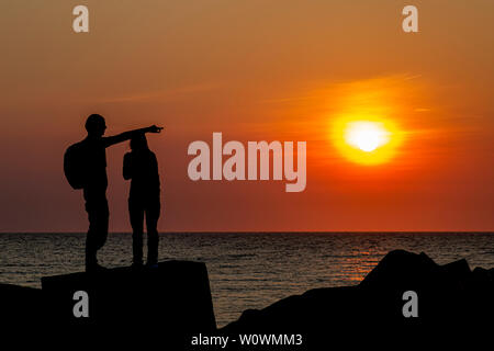 Die Silhouette eines jungen Paares auf der Betonpfeiler schutz Bausteine in Scheveningen unter einem leuchtenden Sonnenuntergang moment, Den Haag, Niederlande Stockfoto