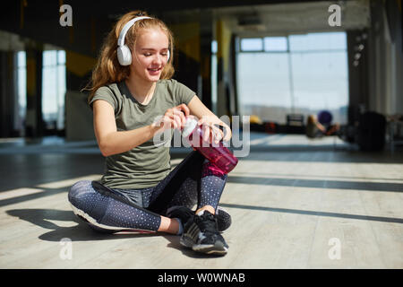 Mädchen in Ihrem Fitnessstudio Verschleiß sitzt auf dem Boden und trinken Wasser aus dem rosa Flasche. Stockfoto