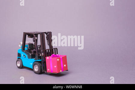 Blau Gabelstapler trägt eine rosa Geschenkbox mit Schleife. Kauf und Lieferung eines präsentieren. Einzelhandel, Rabatte und Wettbewerbe. Wettbewerb Werbeaktionen. Erhöht Stockfoto