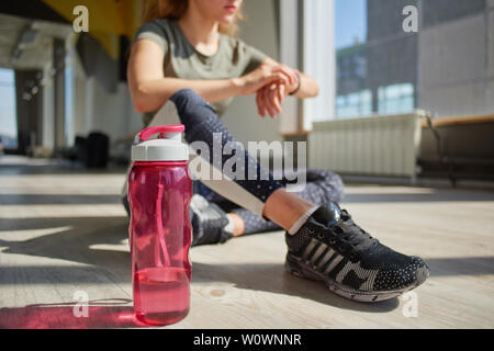 Mädchen in Ihrem Fitnessstudio Verschleiß sitzt auf dem Boden und prüft auf ihre Uhr. Stockfoto