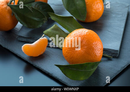 Mandarinen mit Blättern, die auf dem dunklen Schiefer platte Hintergrund. Selektiver Fokus Stockfoto