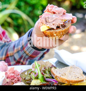 Mann mit einem frischen Salat Plowmans Brötchen gefüllt mit Käse, Gurke und Schinken Stockfoto