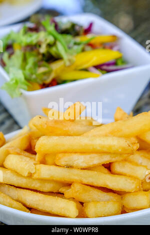 Schüssel mit frisch gebratenen knusprige Chips mit einer gemischten Garten Salat hinter Stockfoto