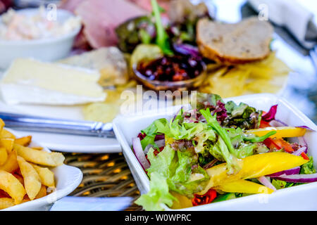 Schüssel Pommes und ein Plowmans Mittagessen mit Salat auf einem Tisch im Sommer. Stockfoto