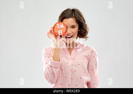 Glückliche junge Frau im Pyjama mit Wecker Stockfoto
