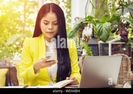 Porträt der Schönen und zuversichtlich Asian Business Frau sitzen vor dem Notebook Laptop und Telefon für Termin update am Arbeitsplatz Stockfoto