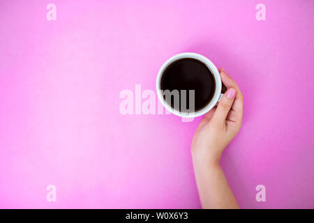 Flatlay mit schwarzer Kaffee in weisser Tasse auf einem rosa Hintergrund. Woman's Hand mit Maniküre sanft Holding Cup. Kopieren Sie Platz. Stockfoto