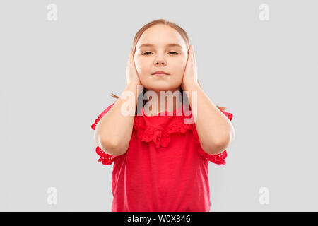 Schöne Mädchen im roten Hemd schließen Ohren durch Hände Stockfoto