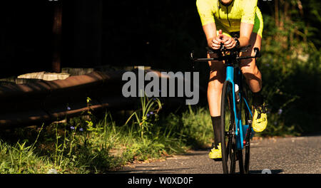 Kopf auf Sicht des Menschen Training auf seinem Rennrad in er am frühen Morgen erleuchtet von Sonnenschein als reitet er aus dem Schatten. Stockfoto