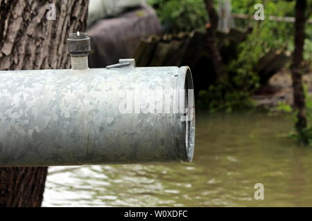 Großer Durchmesser starke Metallrohr mit fehlenden Regelventil oben neben alten Baum verwendet, mit denen das Eindringen von Hochwasser Hinterhof über sandbox Schutz zu Pumpe Stockfoto