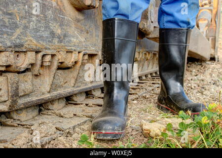 Ein Baggerfahrer steht mit seiner staubigen, schwarze Gummistiefel vor der Stahl seine Caterpillar bulldozer. Stockfoto