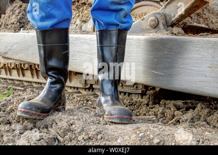 Gummistiefel für die Arbeit verwenden. Ein Baggerfahrer steht mit seiner staubigen Gummistiefel vor der Stahl seine Caterpillar bulldozer. Stockfoto