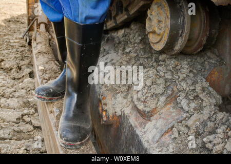 Gummistiefel für die Arbeit verwenden. Ein Baggerfahrer steht mit seiner staubigen Gummistiefel auf dem Laufwerk chaint seiner Planierraupe. Stockfoto