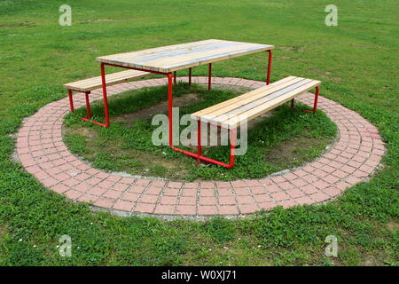 Öffentlicher Park Tisch mit zwei Bänken aus verfallenen Holz und Metall mit dekorativen Steine und ungeschnittenes Gras umgeben angeschlossen Stockfoto