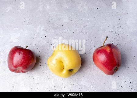 Drei hässliche Rote und gelbe Äpfel liegen in Reihe auf grauem Beton Hintergrund. Abfälle zero Konzept. Ansicht von oben, flach, kopieren. Stockfoto