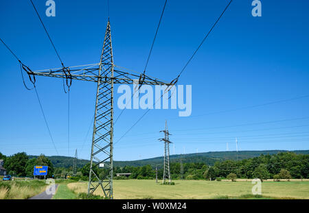 Zwei hohe strommasten gegen den blauen Himmel in einer wunderschönen ländlichen Sommer Landschaft mit Windkraftanlagen im Hintergrund Stockfoto