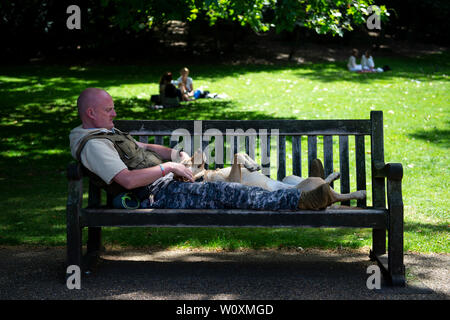 Ein Mann nimmt einen Bruch von der Hitze mit seinem Hund in St. James Park in London. Stockfoto