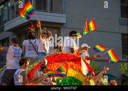 NEW YORK CITY - 25 Juni, 2017: Teilnehmer, die das Tragen von T-Shirts durch die Marken Wyndham und Barclays wave Flags auf einen Schwimmer in der Gay Pride Parade gefördert. Stockfoto