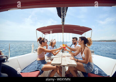 Glückliche Menschen toasten Getränke auf der Yacht deck und Lachen. Freundliche Männer und Frau Party auf einem Boot. Stockfoto