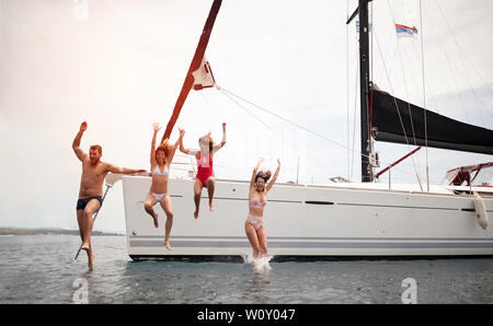 Freunde springen von Segelboot in See. Junge Menschen Spaß auf der Yacht haben. Stockfoto