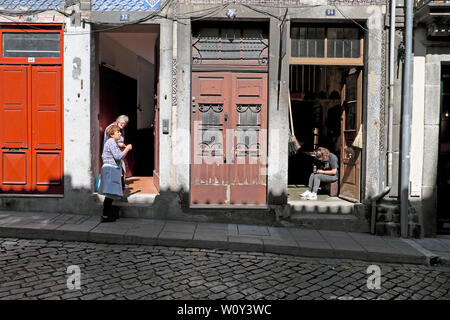 Porto Nachbarn zwei alte Frauen chatten vor der Tür und junge Frau sitzt durch die offene Tür der Shop in einer Straße in Porto Portugal Europa KATHY DEWITT Stockfoto