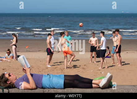 Portobello, Schottland, Großbritannien. 28 Juni, 2019. Warme Temperaturen und ununterbrochenen Sonnenschein brachte Hunderte von Menschen und Familien diesem berühmten Strand ausserhalb von Edinburgh zu genießen. Jugendliche spielen mit Fußball am Strand und eine Frau mit einem Buch entspannen. Credit: Iain Masterton/Alamy leben Nachrichten Stockfoto