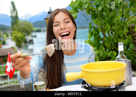 Schweizer Käsefondue. Frau lachend angezeigt und essen Brot mit geschmolzenem Käse. Traditionelle Speisen aus der Schweiz. Menschen Spaß am See in den Alpen auf Reisen in Europa. Stockfoto