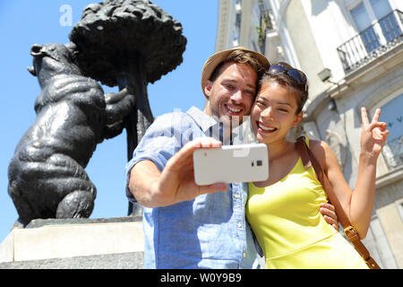 Touristen nehmen selfie Foto Bilder von berühmten Bären Statue in Madrid auf der Puerta del Sol. Junges Paar mit Smartphone Kamera auf touristische Attraktion und der madrono Baum, Symbol von Madrid, Spanien. Stockfoto