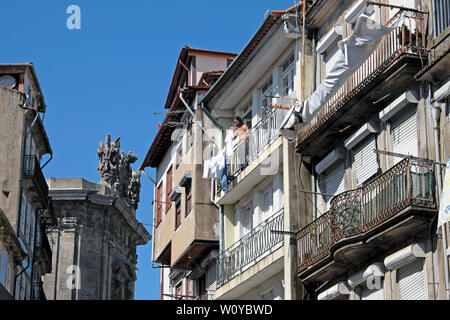 Ein Mensch außerhalb seiner Wäsche aufhängen an einem Mehrfamilienhaus, Balkon Wäscheleine auf einer Straße in der Stadt Porto Oporto Portugal Europa KATHY DEWITT Stockfoto