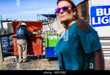 Puerto Peñasco, Sonora, 20. Oktober 2017. - Zwei amerikanische Frauen Touristen schlendern, um die touristische Dock von Puerto Peñasco während Kann ein erwachsener Mann der extremen Armut Sucht nach Essen, das im Papierkorb Inhalt. Dos mujeres Turistas norteamericanas pasean Por El Muelle Turístico de Puerto Peñasco un hombre mientras adulto mayo de pobreza Extrema busca comida Dentro De Los contenidos de basura. (Foto: Luis Gutierrez/NortePhoto.com) Stockfoto