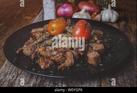 Teilstücke von Rindfleisch Steak vom Grill mit Gewürzen würzen und Tomate auf schwarze Platte mit grauen und dunklen Ton Beleuchtung. Stockfoto