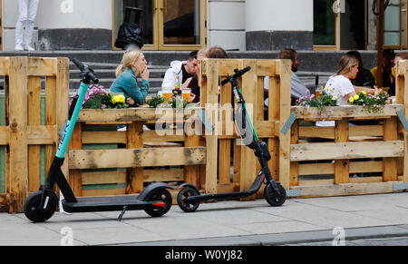 Oslo, Norwegen - 20. Juni 2019: Geparkte elektrisch angetriebene push Roller vor ein Restaurant im Freien mit Europa Paletten eingezäunt. Stockfoto