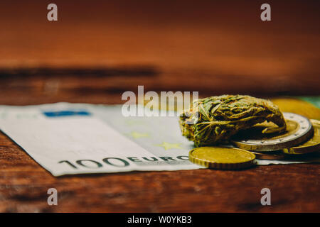 Ein Cannabis bud liegt auf einem hundert Euro Bill und Münzen. Kauf und Verkauf der Legalisierung weicher Drogen. medizinischen Cannabis Geschäftskonzept. Stockfoto