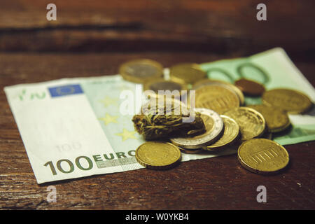 Ein Cannabis bud liegt auf einem hundert Euro Bill und Münzen. Kauf und Verkauf der Legalisierung weicher Drogen. medizinischen Cannabis Geschäftskonzept. Stockfoto